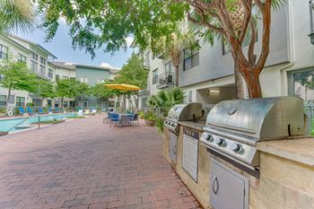 A brick patio with a grill and a pool in the background.